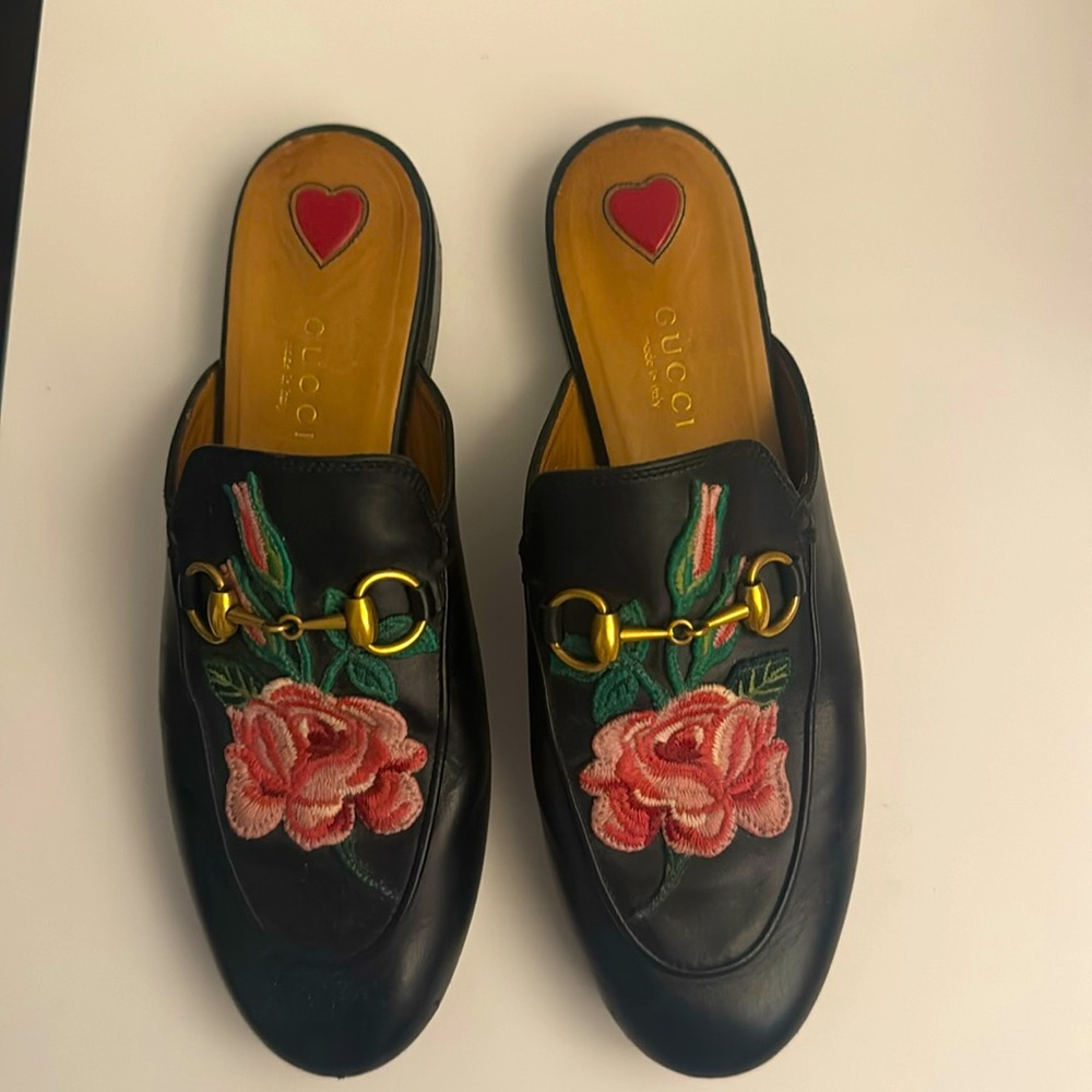 Black Gucci mules with a flower on it.